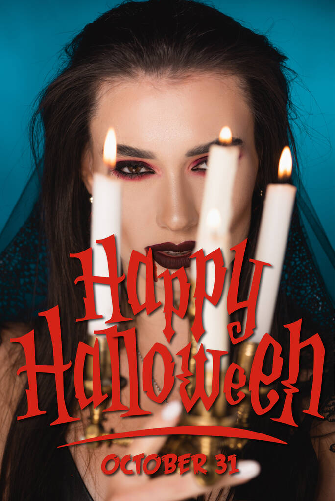 mladá žena v závoji s krví na obličeji v blízkosti hořících svíček a šťastný halloween nápis na modré - Fotografie, Obrázek