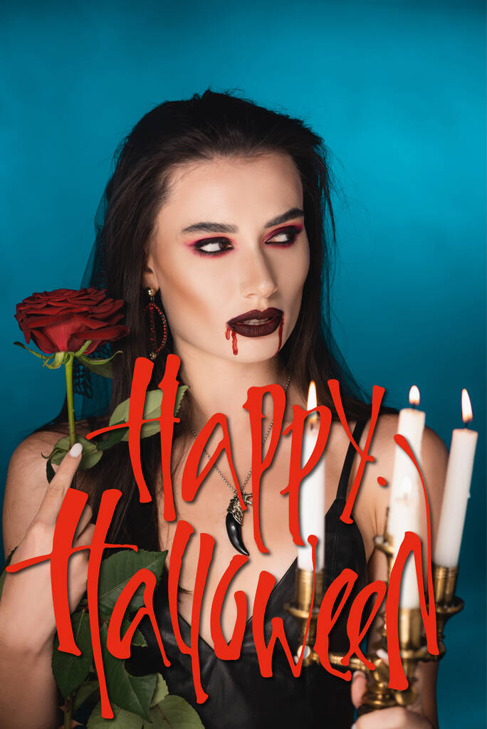 jovem mulher com sangue no rosto perto de velas ardentes, rosa e feliz halloween lettering em azul - Foto, Imagem