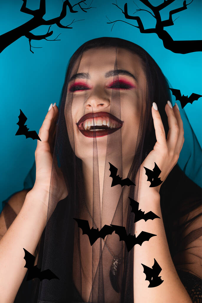 evil woman with black makeup, closed eyes and veil laughing near illustration on blue - Photo, Image