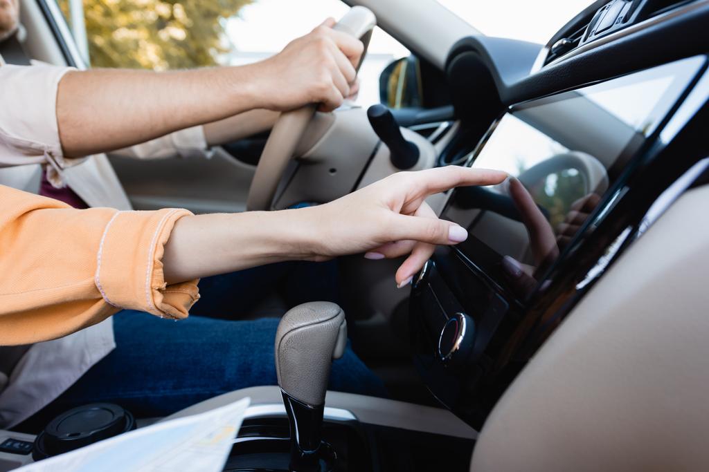 Περικοπή άποψη της γυναίκας που χρησιμοποιούν ακουστικό σύστημα στο αυτοκίνητο, ενώ ο σύζυγος οδήγηση σε θολή φόντο  - Φωτογραφία, εικόνα