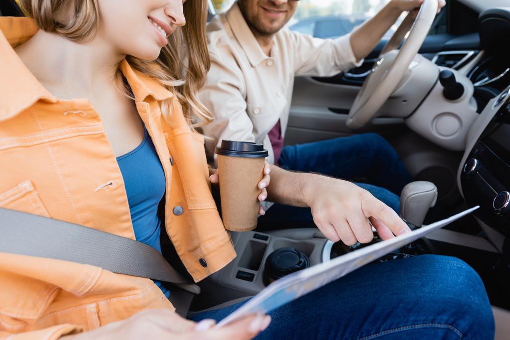 Обрезанный вид мужчины, указывающего на карту рядом с улыбающейся женой с кофе, чтобы поехать в машине  - Фото, изображение