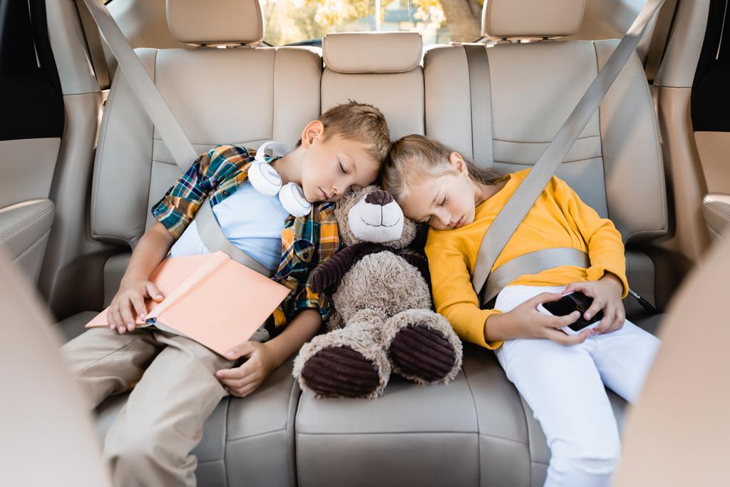 Enfants avec smartphone, livre et jouet doux dormant en auto pendant le voyage - Photo, image