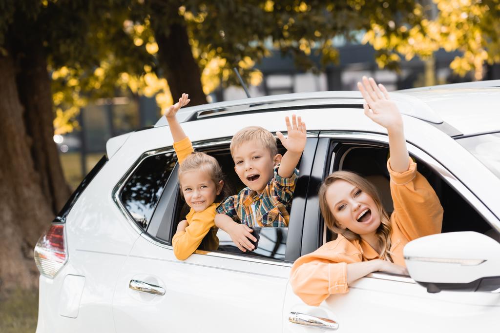 Glimlachende kinderen zwaaien handen in de buurt van moeder tijdens het reizen met de auto  - Foto, afbeelding