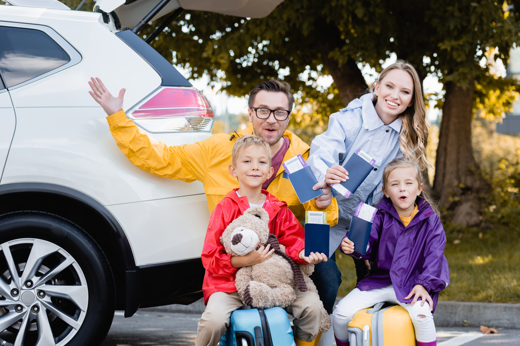 Família alegre segurando passaportes com passagens aéreas perto do carro ao ar livre  - Foto, Imagem