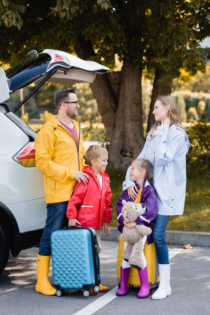 Sonbahar kıyafetli gülen aile, dışarıda arabanın yanında duran bavullar.  - Fotoğraf, Görsel