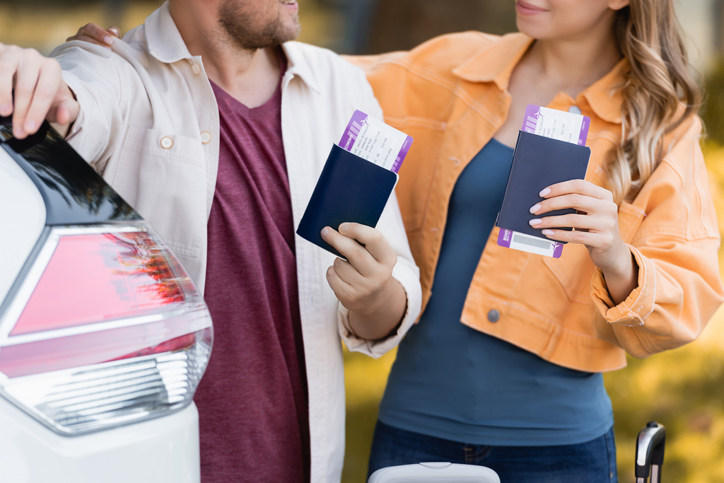 Vista recortada de la mujer con pasaporte y billete de avión abrazando marido cerca de coche al aire libre  - Foto, imagen
