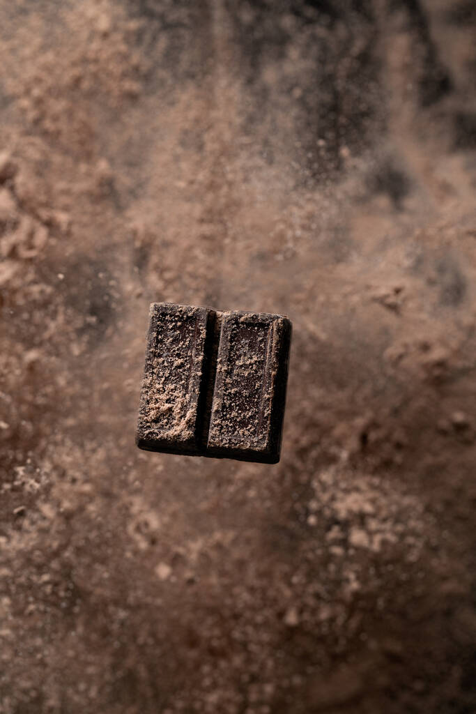 Een oppere uitzicht opname van een donker chocoladestuk besprenkeld met cacaopoeder - Foto, afbeelding