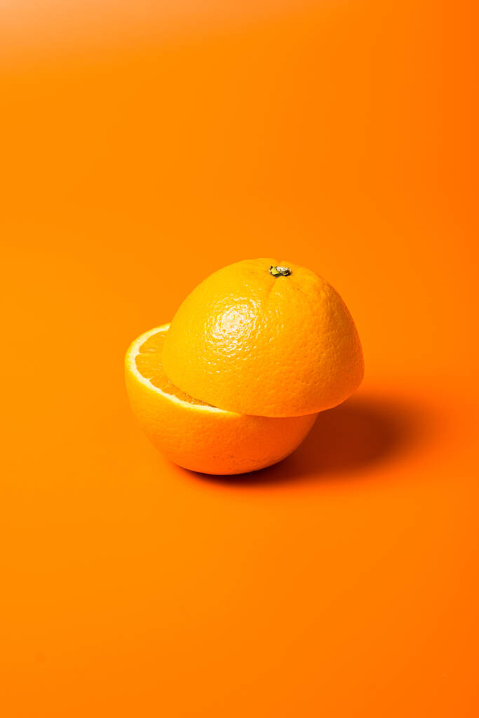 Ένα κάθετο πλάνο από ένα ζουμερό μισοκομμένο πορτοκάλι σε πορτοκαλί φόντο - Φωτογραφία, εικόνα