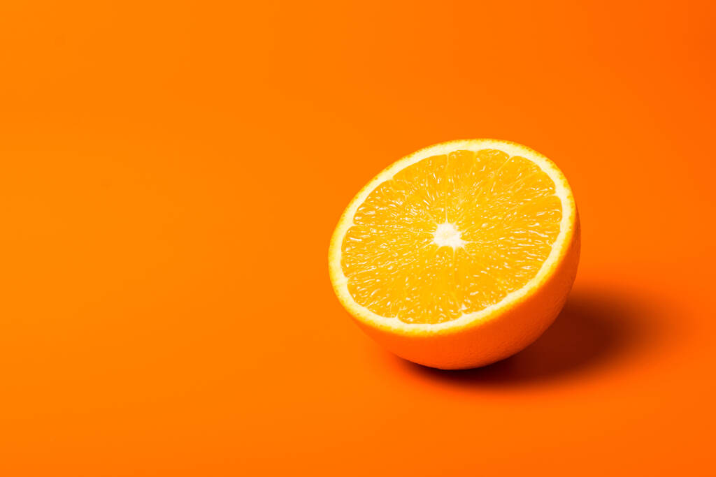 Un primer plano de una jugosa mitad naranja cortada sobre fondo naranja - Foto, imagen