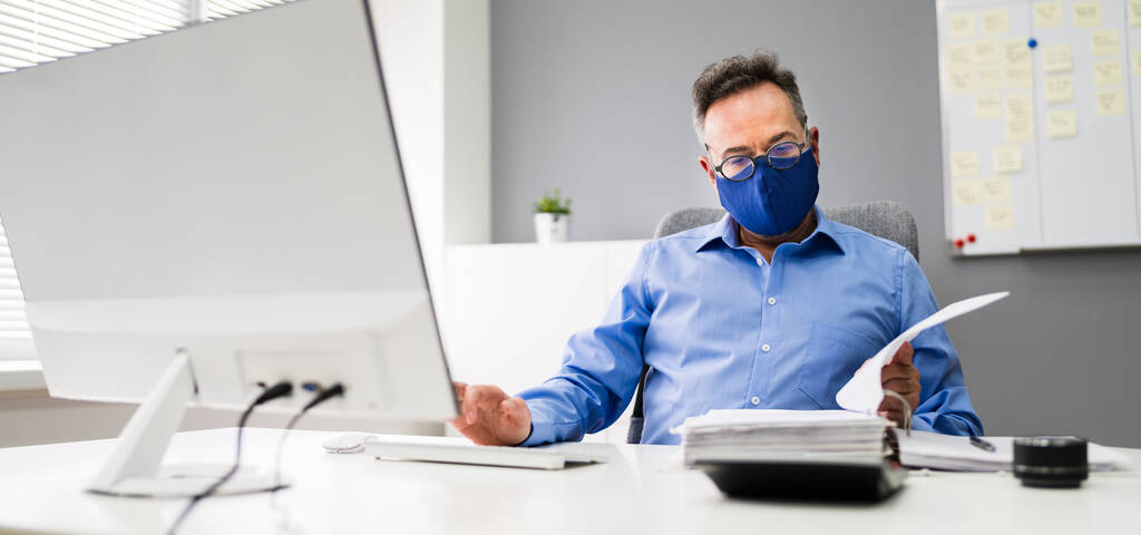 Empregado do negócio mais velho que trabalha no computador que veste a máscara facial - Foto, Imagem