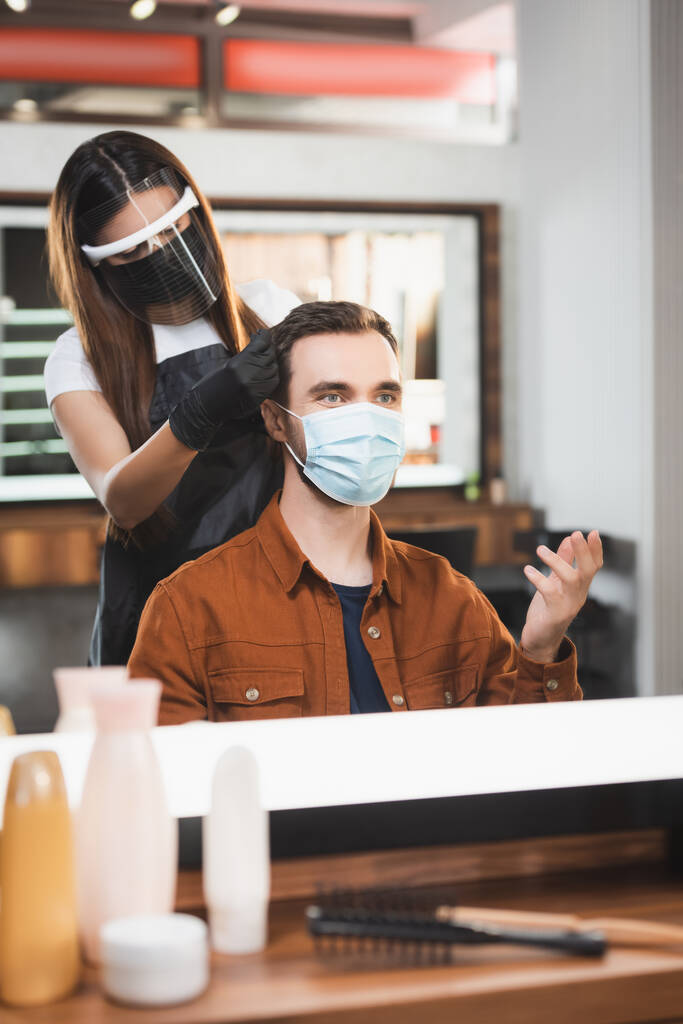зеркальное отражение жеста человека в медицинской маске и парикмахера в щит для лица, стригущего волосы - Фото, изображение