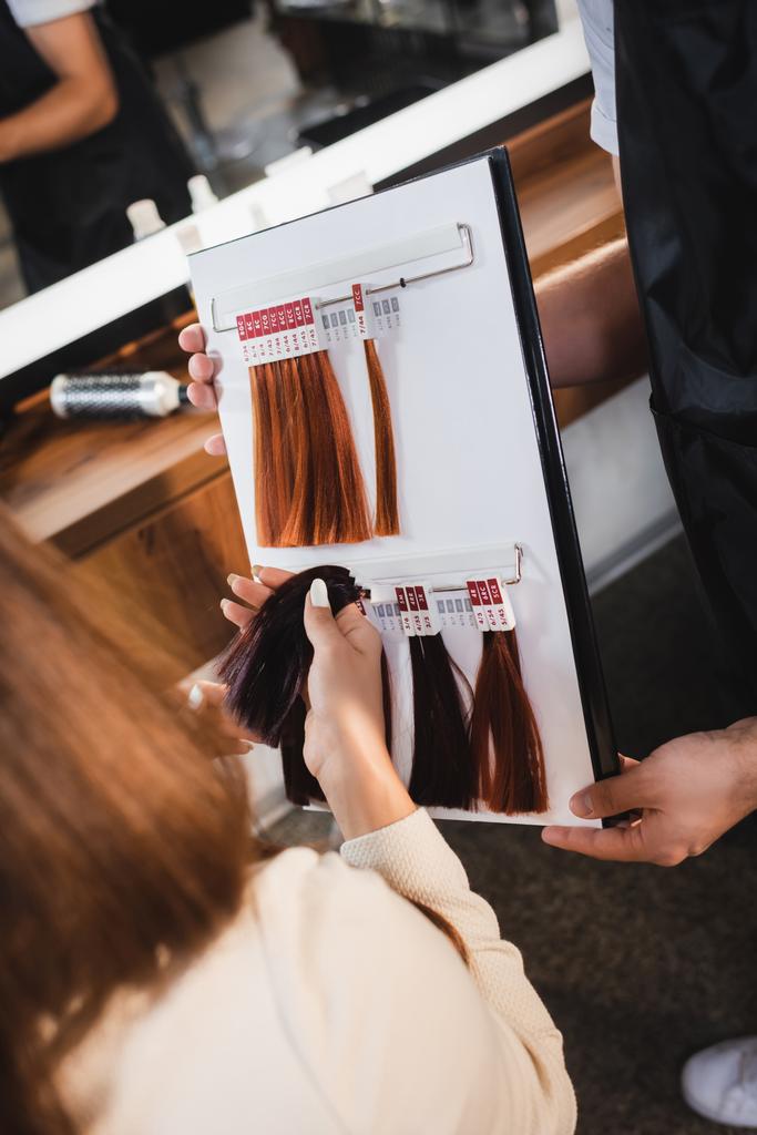 обрізаний вид перукаря, що тримає палітру кольорів волосся біля клієнта, торкаючись зразка на розмитому передньому плані
 - Фото, зображення
