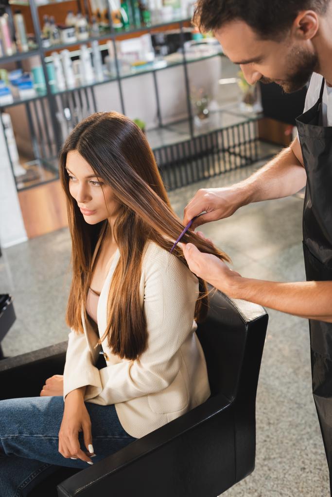 молодой парикмахер расчесывает волосы женщины в парикмахерской - Фото, изображение