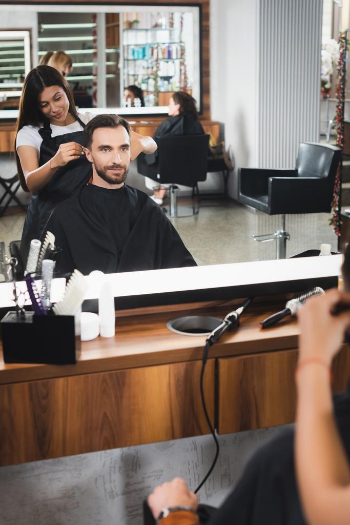 specchio riflesso di giovane barbiere taglio capelli di uomo barbuto, primo piano sfocato - Foto, immagini