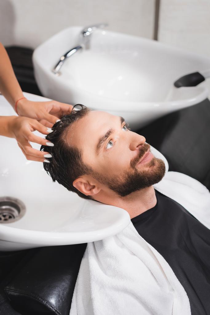 holič mytí vlasů mladého vousatého muže v salonu krásy - Fotografie, Obrázek