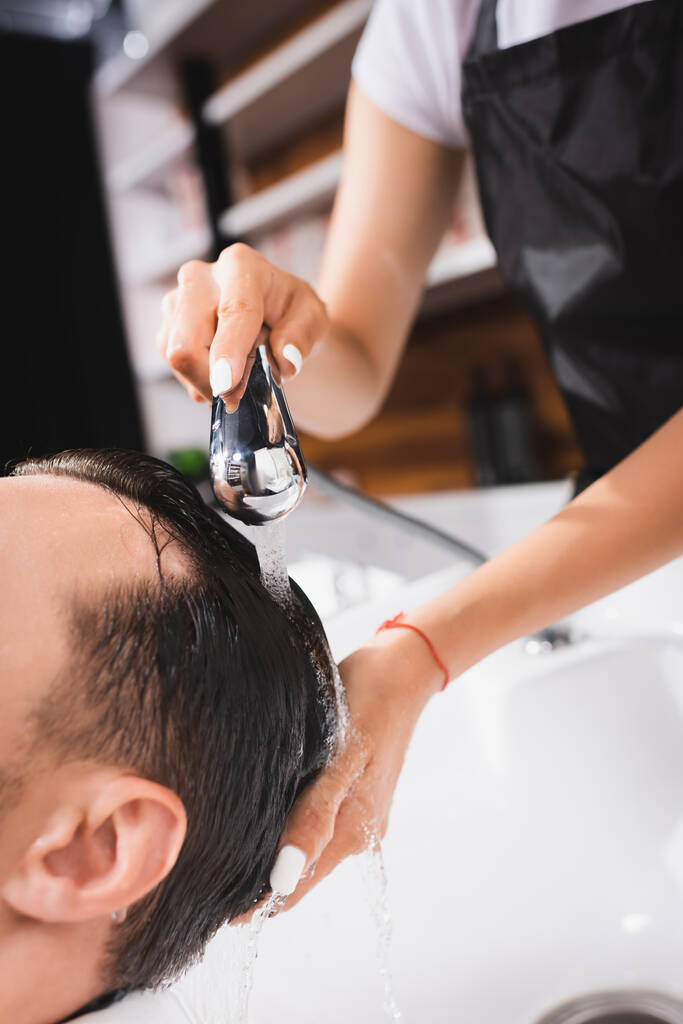 vista ritagliata di barbiere che lava capelli di cliente in salone di bellezza - Foto, immagini