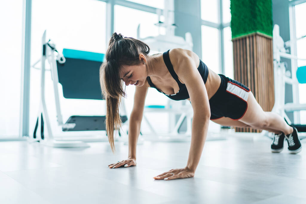 Полное тело стройная сильная женщина в спортивной одежде делает отжимания на полу в современном легком тренажерном зале во время интенсивной тренировки - Фото, изображение