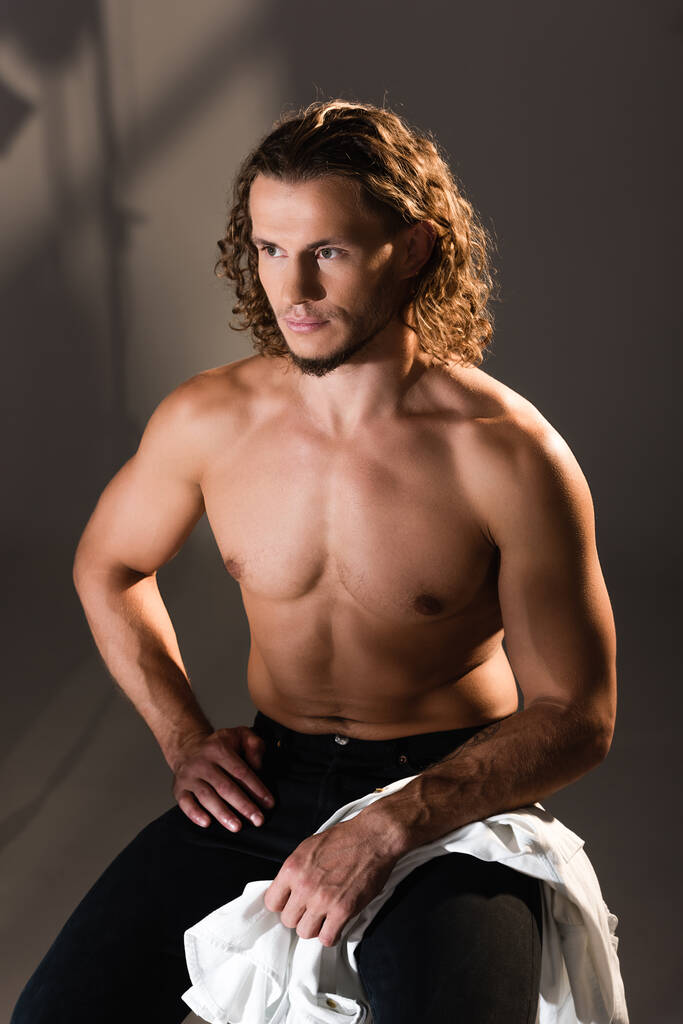 сексуальный мужчина без рубашки с длинными волосами позирует на темном фоне - Фото, изображение