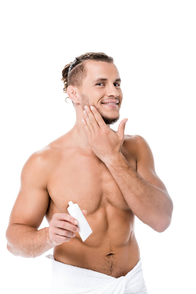 усміхнений сексуальний без сорочки чоловік в рушнику наносить крем для обличчя ізольований на білому
 - Фото, зображення