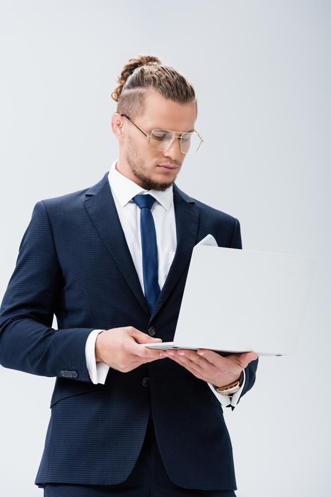 νεαρός επιχειρηματίας με κοστούμι και γυαλιά με φορητό υπολογιστή απομονωμένο σε λευκό - Φωτογραφία, εικόνα