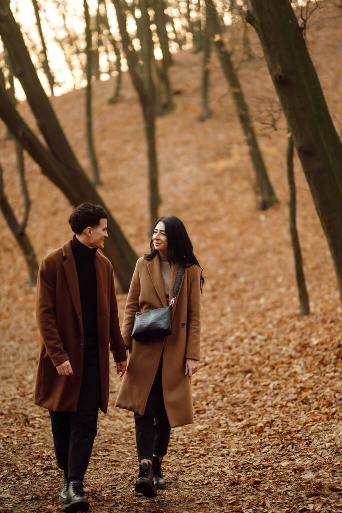 Młoda para zakochana trzymająca się za ręce i przechadzająca się przez las w jesienny dzień. Piękna stylowa para ciesząca się jesienną pogodą w parku. Koncepcja młodości, miłości, wolności. - Zdjęcie, obraz