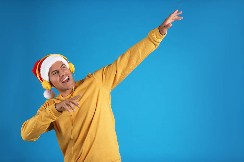 Эмоциональный человек с наушниками на синем фоне, место для текста. Рождественская музыка - Фото, изображение