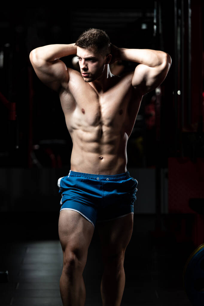 Jongeman staat sterk in de Gym en Flexing Muscles - Muscular Athletic Bodybuilder Fitness Model Poseren na oefeningen - Foto, afbeelding