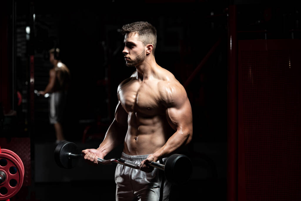 Atleta en el gimnasio realizando rizos de bíceps con una barra - Foto, Imagen