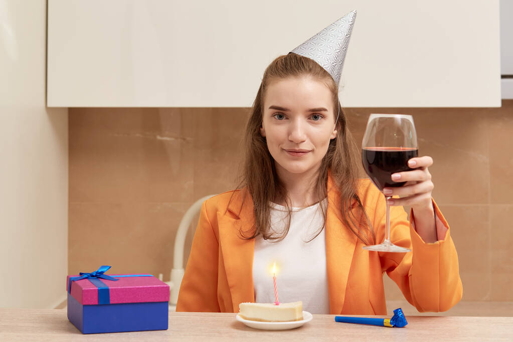 Una mujer hace un brindis. En la mesa hay un pastel de cumpleaños con una vela encendida. - Foto, imagen
