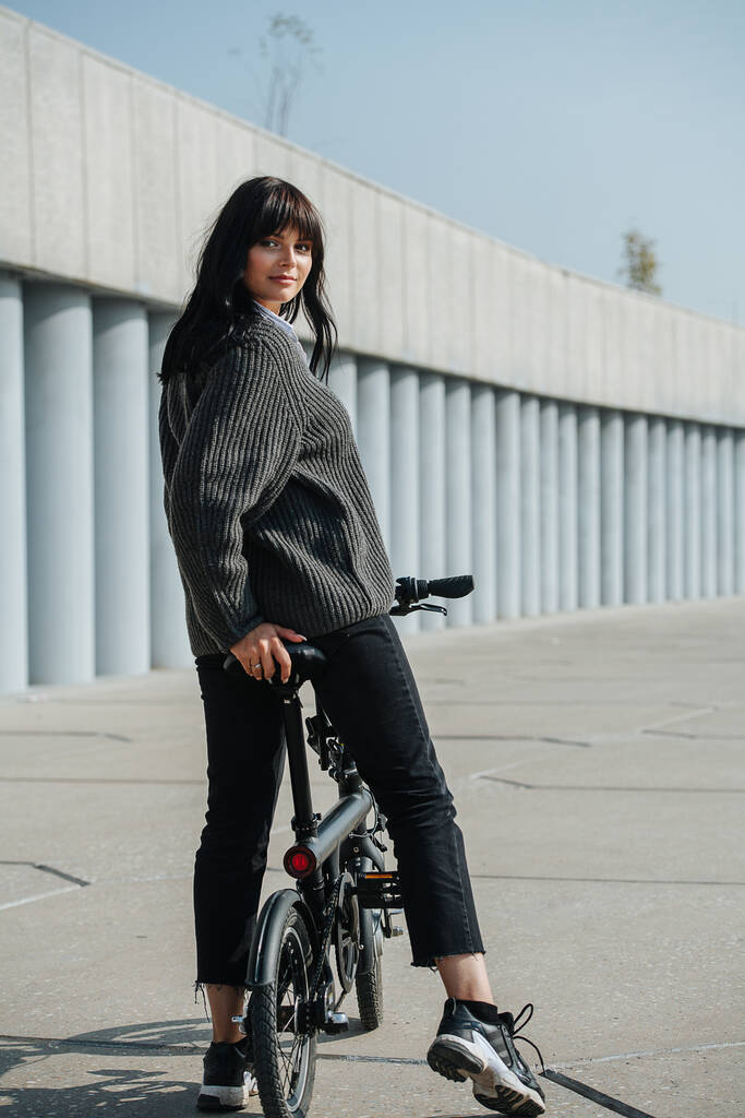 Beautiful black-haired woman sitting on ebike, looking over shoulder at camera - Photo, Image