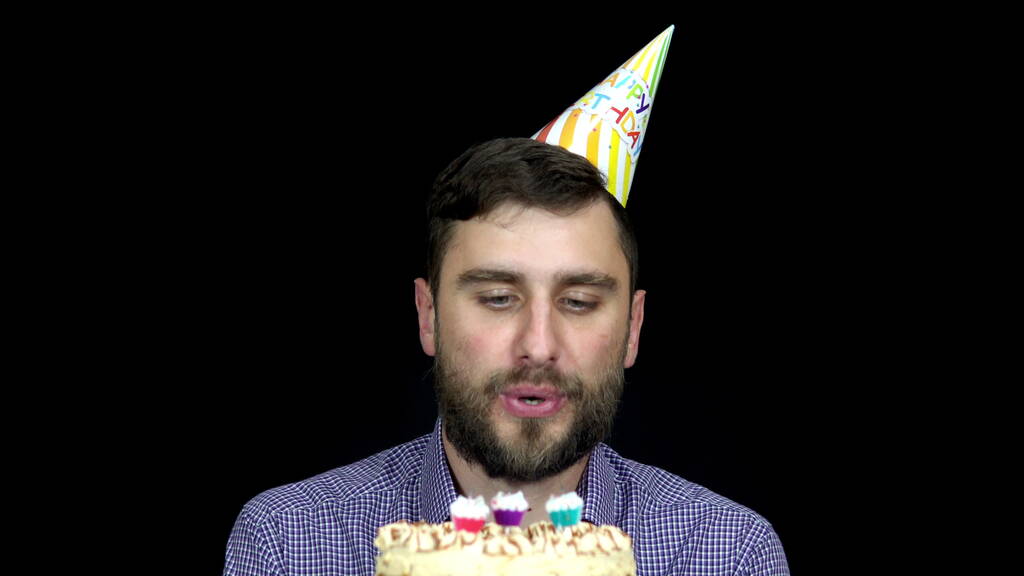 Mężczyzna w urodzinowej czapce zdmuchuje świeczki na torcie 4k - Zdjęcie, obraz