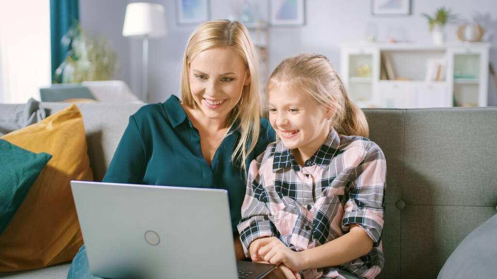 美しい若いお母さんと彼女のかわいい娘は自宅でソファに座っている間、ラップトップを使用します。家族は一緒にコンピュータでビデオや漫画を見て時間を過ごす. - 写真・画像