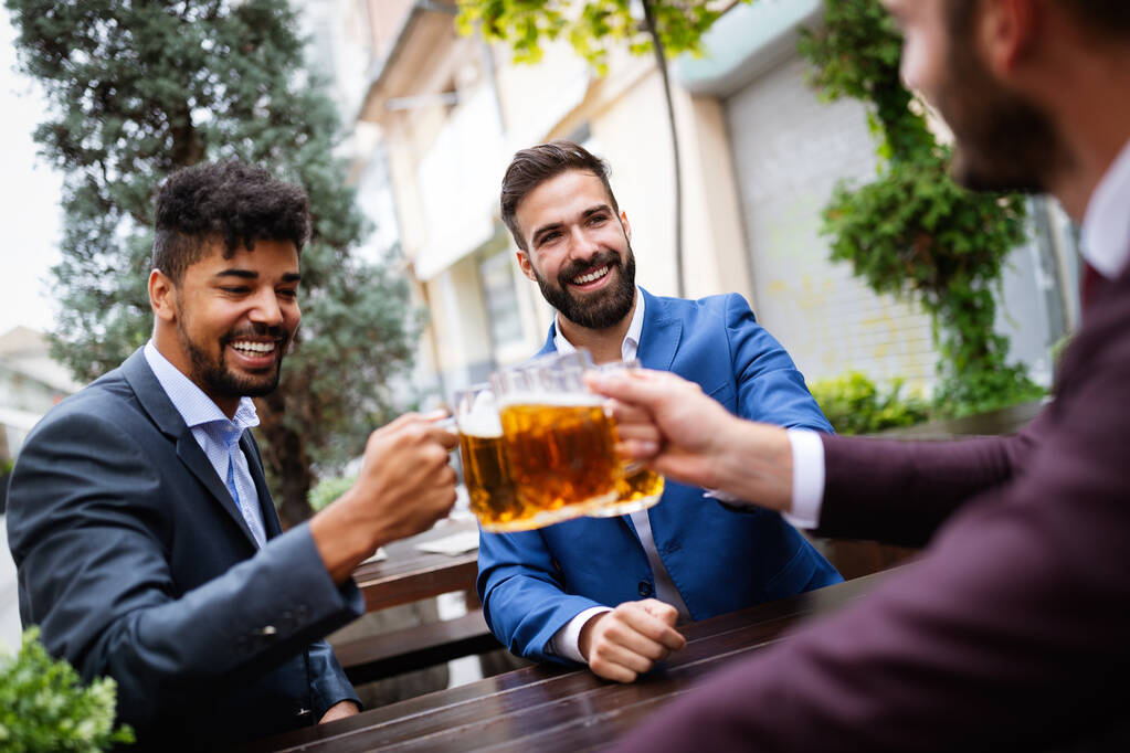 Jóvenes empresarios guapos bebiendo cerveza, hablando y sonriendo mientras descansan en el pub - Foto, imagen