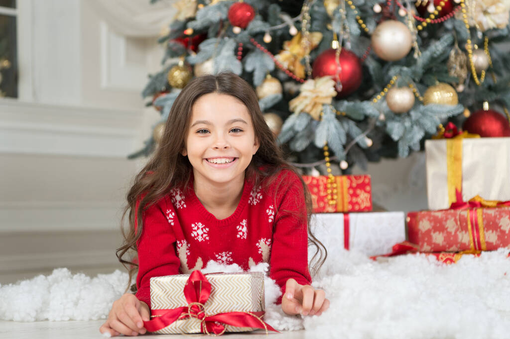 Feliz sonrisa de niño pequeño con la caja presente acostado en la nieve artificial en el árbol de Navidad, año nuevo - Foto, Imagen