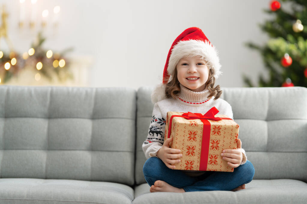 Счастливого Рождества и Рождества! Веселая милая девочка с подарком. Парень веселится рядом с деревом..     - Фото, изображение