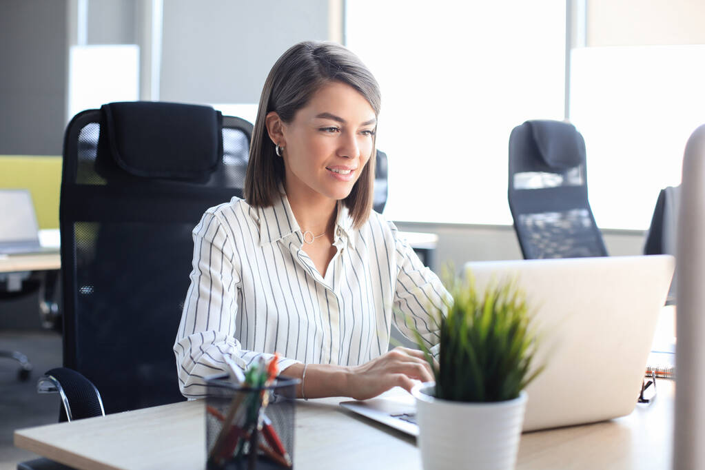 Красивая деловая женщина в элегантной повседневной одежде работает на ноутбуке в офисе. - Фото, изображение