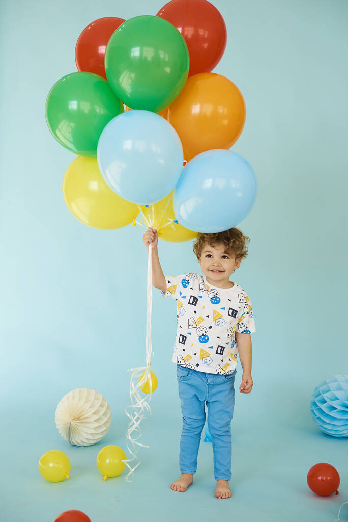 Πλήρες μήκος πορτρέτο του χαρούμενου αγοριού κρατώντας μπαλόνια ποζάρουν σε μπλε φόντο - Φωτογραφία, εικόνα
