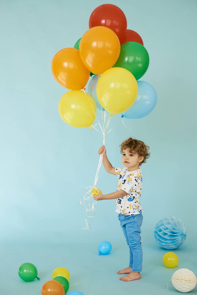Retrato de cuerpo entero de niño alegre sosteniendo balones posando sobre fondo azul - Foto, imagen