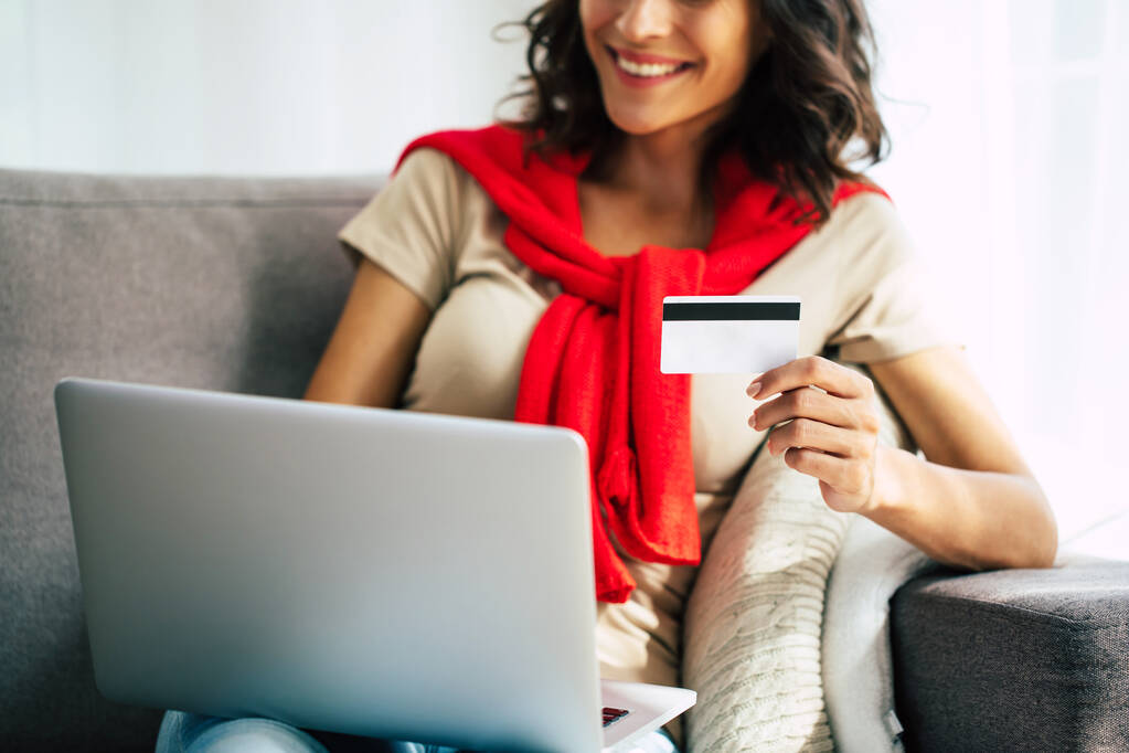 Gyönyörű boldog fiatal nő alkalmi ruhák ül a kanapén otthon, és csinál online vásárlás fekete pénteken. - Fotó, kép