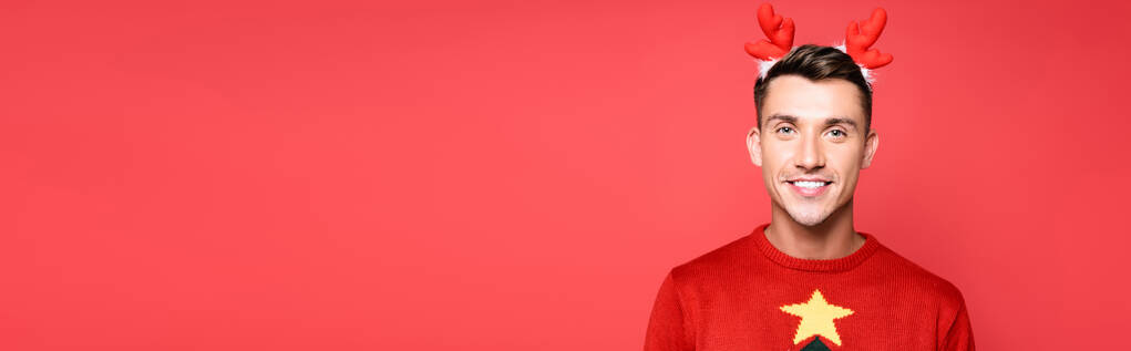 Feliz hombre adulto joven con aro en la cabeza mirando a la cámara aislada en rojo, pancarta - Foto, Imagen