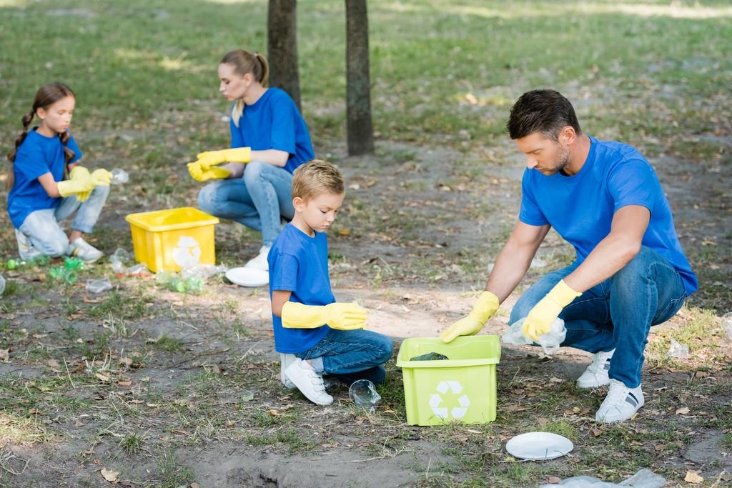 rodzina wolontariuszy zbierających plastikowe śmieci w pojemnikach z symbolem recyklingu, koncepcja ekologii - Zdjęcie, obraz
