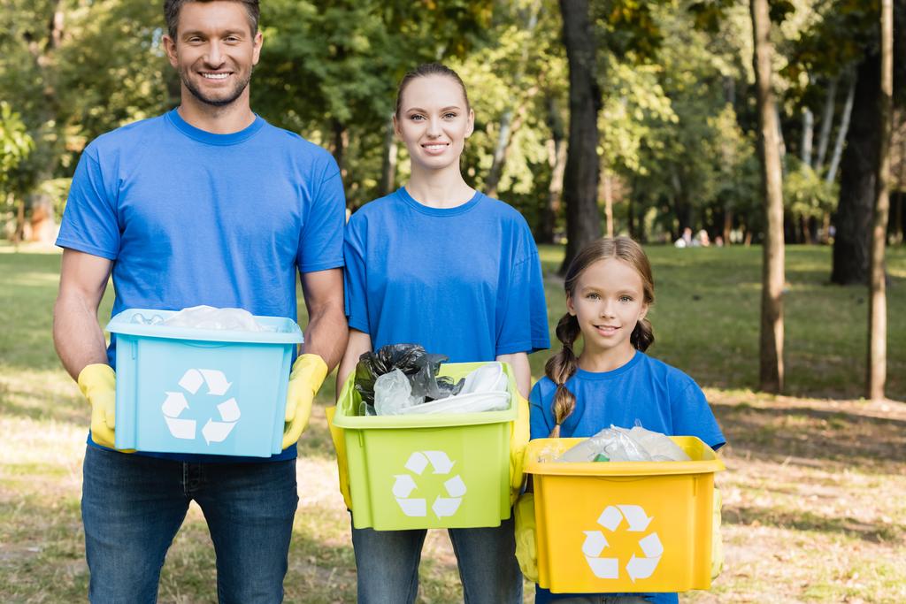 familia sonriente sosteniendo contenedores con símbolos de reciclaje, llenos de residuos plásticos, concepto de ecología - Foto, imagen