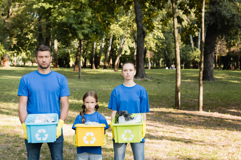 familia de voluntarios sosteniendo contenedores con símbolos de reciclaje, llenos de residuos plásticos, concepto de ecología - Foto, Imagen