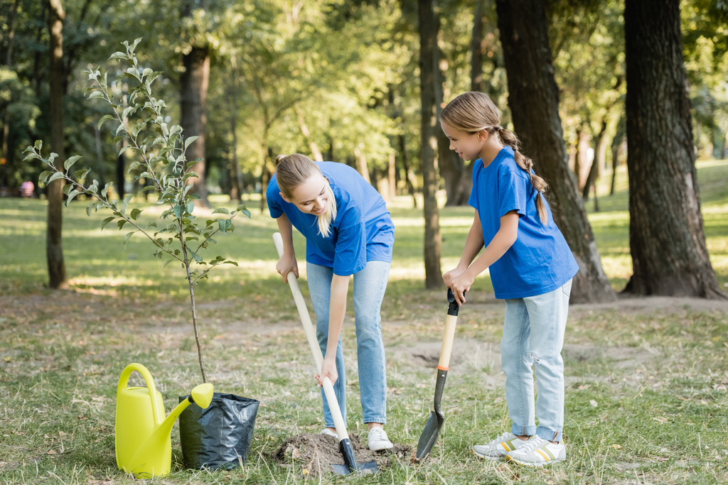 mother and daughter digging ground with shovels near watering can and seedling, ecology concept - Photo, Image