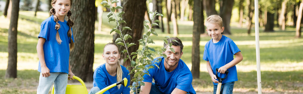 familia feliz de voluntarios plantando árbol joven en el bosque, concepto de ecología, bandera - Foto, imagen
