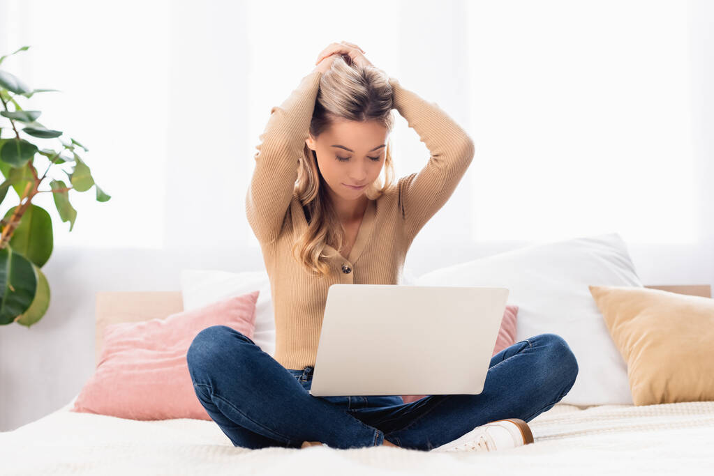 Freelancer jovem com as mãos perto da cabeça usando laptop na cama  - Foto, Imagem