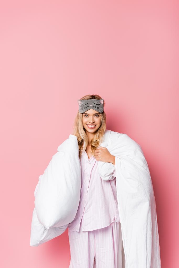Χαρούμενη γυναίκα με πιτζάμες και καλυμμένη με δεμένα μάτια κουβέρτα σε ροζ φόντο - Φωτογραφία, εικόνα