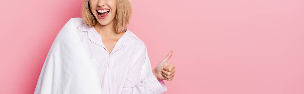 Vue recadrée de femme gaie en pyjama et couverture montrant comme sur fond rose, bannière  - Photo, image