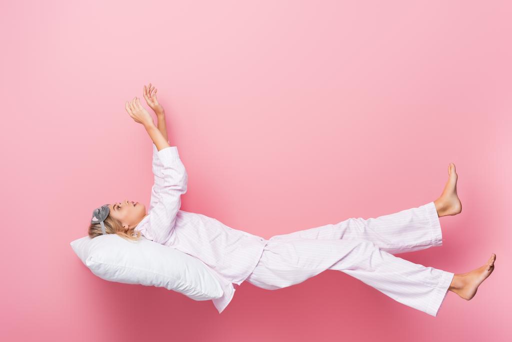 Νεαρή γυναίκα με πιτζάμες ξαπλωμένη στο μαξιλάρι σε ροζ φόντο - Φωτογραφία, εικόνα
