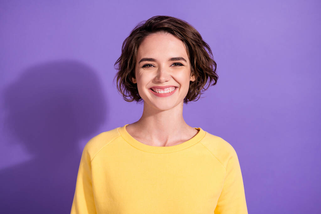 Portré szép lány néz ki a kamera fogas mosoly visel fényes pulóver elszigetelt felett lila színű háttér - Fotó, kép